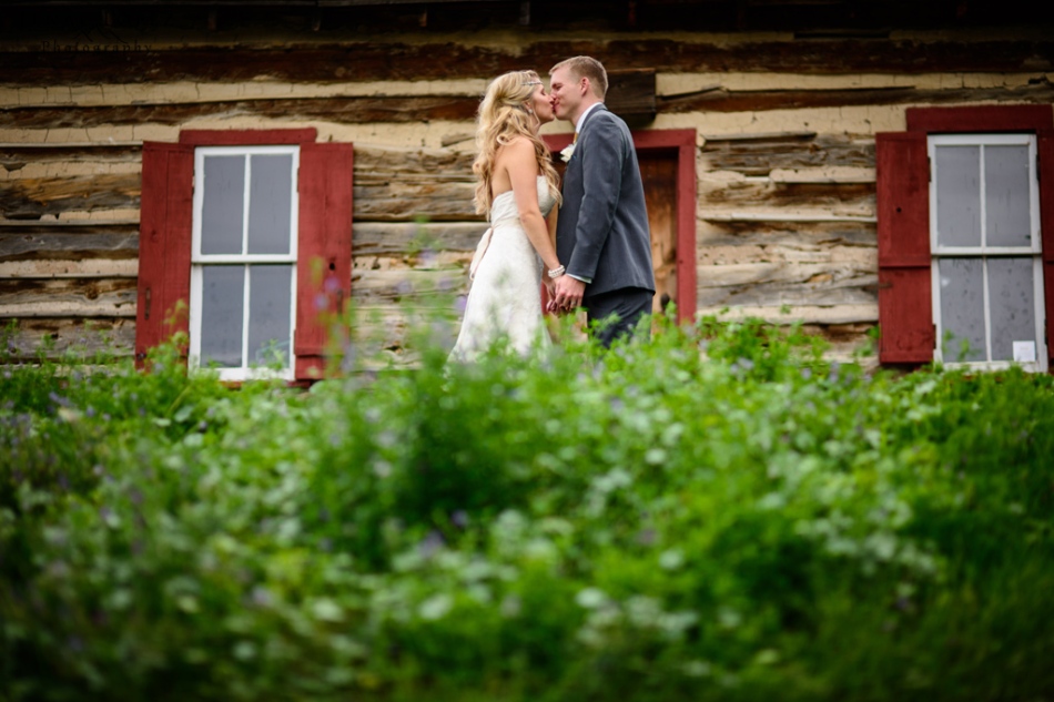 bride and groom kiss in front of old cabin in colorado mountains
